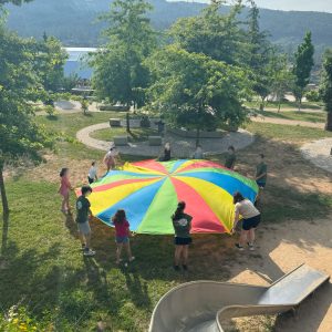 Grupo de participantes realizando xogos cooperativos con paracaídas ao aire libre durante unha actividade de animación sociocultural.